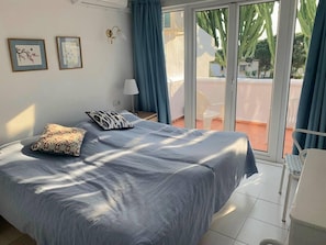 A bedroom with a large bed, a nightstand, a lamp, and a view of the outside balcony. - Calahonda - Sleeps 6 - Parking - Garden - Pool (Mijas)