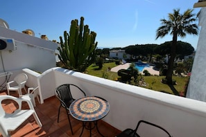 A balcony with a tiled table and chairs, a view of a swimming pool, and a large cactus. - Calahonda - Sleeps 6 - Parking - Garden - Pool (Mijas)