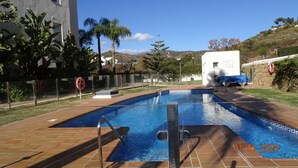 A swimming pool with a lifebuoy, surrounded by a fence, palm trees, and a building in the background. - Elviria 2-bed Apt, Sleeps 4, Pool, 20m to Beach (Marbella)