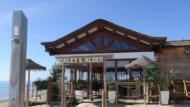 A beachside restaurant named "Alex & Alder" with a wooden facade, large windows, and a sign indicating "Lido Beach". - Elviria 2-bed Apt, Sleeps 4, Pool, 20m to Beach (Marbella)