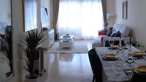 A dining area with a table set for four, a sofa in the background, and a plant in the foreground. - Elviria 2-bed Apt, Sleeps 4, Pool, 20m to Beach (Marbella)