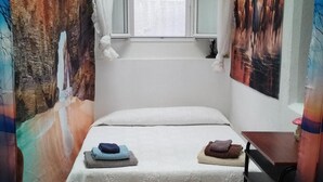 Ein kleines, gemütliches Zimmer mit einem Einzelbett, einem Fenster mit Vorhängen und einem an der Wand hängenden Gemälde.