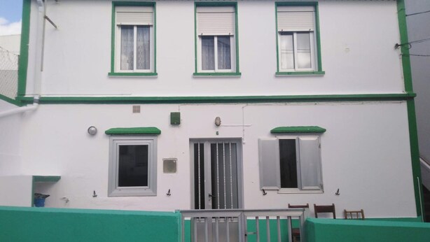 Ein zweistöckiges Gebäude mit Grün-Weiß-Farbgebung, mit drei Fensterläden, einer mittleren Tür und einem kleinen Balkon.