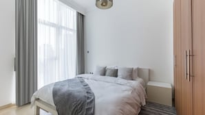A modern bedroom with a bed, bedside tables, a wardrobe, and a large window with curtains. - 1 br in Dorra Bay - Marina View (Dubai)
