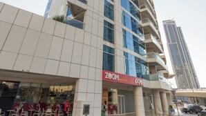 A modern high-rise building with a prominent glass facade, a visible restaurant named "Zoom Market" at the ground level, and a clear sky in the background. - 1 br in Dorra Bay - Marina View (Dubai)