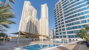 A pool area with lounge chairs and a canopy, surrounded by high-rise buildings. - 1 br in Dorra Bay - Marina View (Dubai)