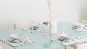 A dining table set with white plates, bowls, glasses, and cutlery. - 1 br in Dorra Bay - Marina View (Dubai)