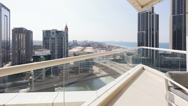 A high-rise building with a glass balcony overlooking a cityscape and a body of water. - 1 br in Dorra Bay - Marina View (Dubai)