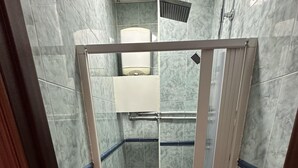 Eine Dusche mit barrierefreiem Einstieg, Glastür, gefliesten Wänden und einer weißen Toilette im Hintergrund.
