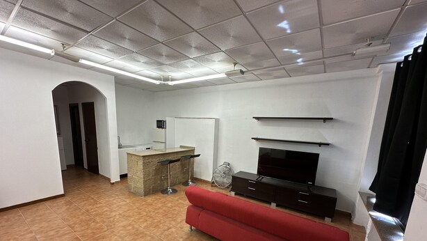 Ein Wohnzimmer mit rotem Sofa, Fernseher, Küchenbereich und einer Decke mit Einbauleuchten.