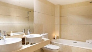 A modern bathroom with two sinks, a toilet, and a bathtub.