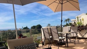 A patio with a sofa, chairs, and an umbrella, overlooking a scenic view.
