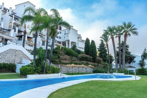 Resort com piscina, palmeiras e um morro com edifícios.