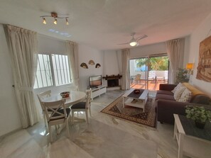 A spacious living room with a dining area, a TV, and a fireplace. There is a sliding glass door leading to an outdoor patio. - Lovely 2-bed Calahonda Apartment sea & Golf Views (Mijas)