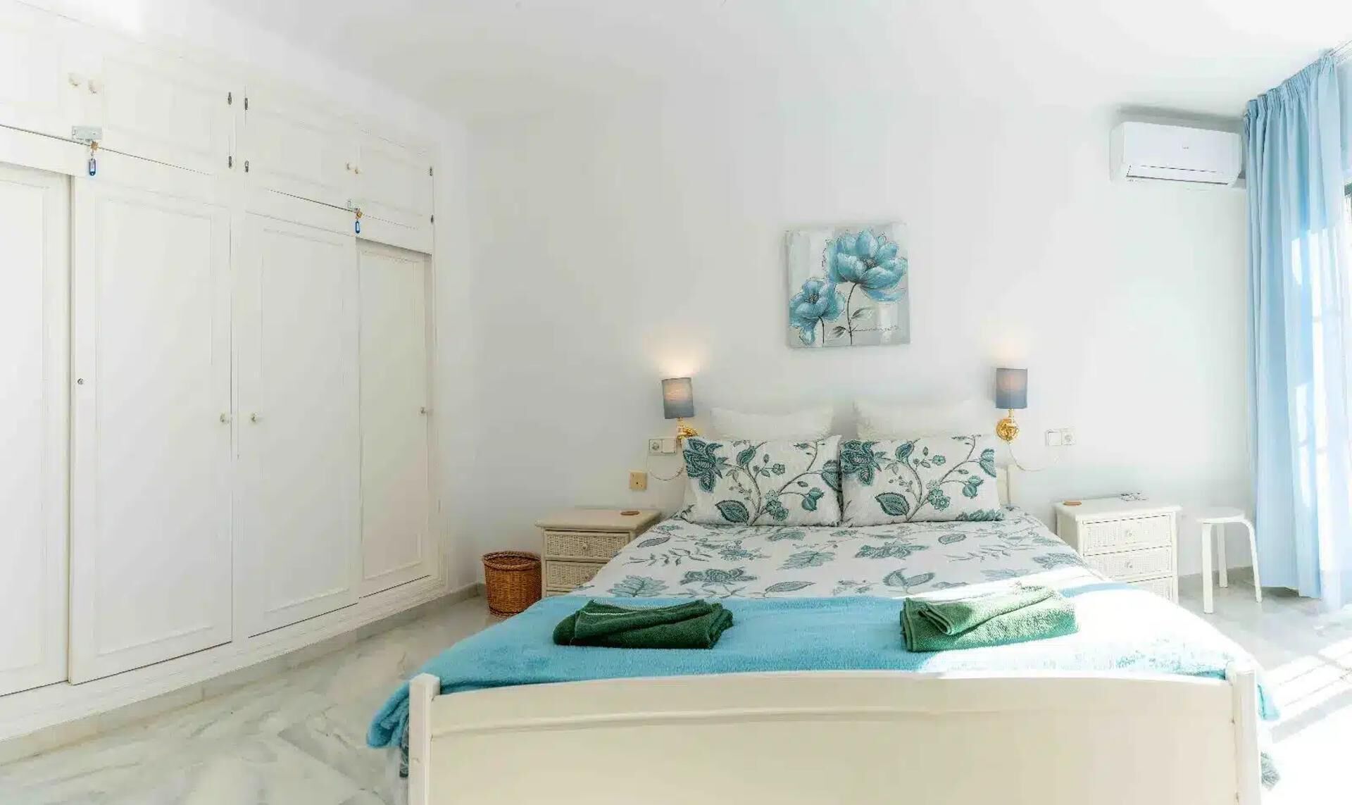 A bedroom with a bed, nightstands, a wall-mounted air conditioner, and a large wardrobe.