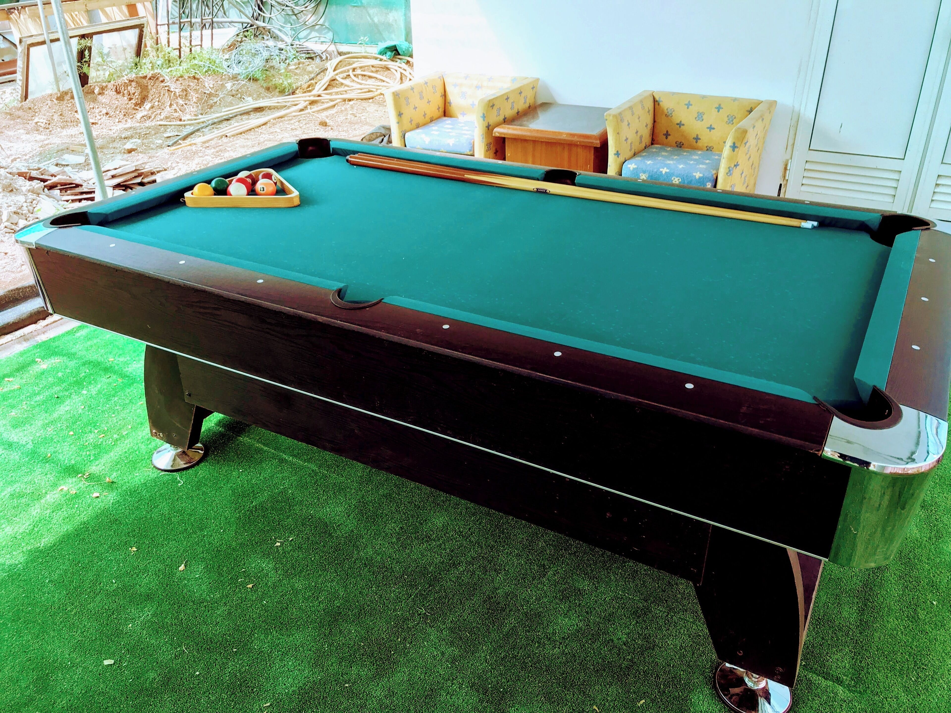 A pool table with a green felt surface, surrounded by a green artificial turf area.