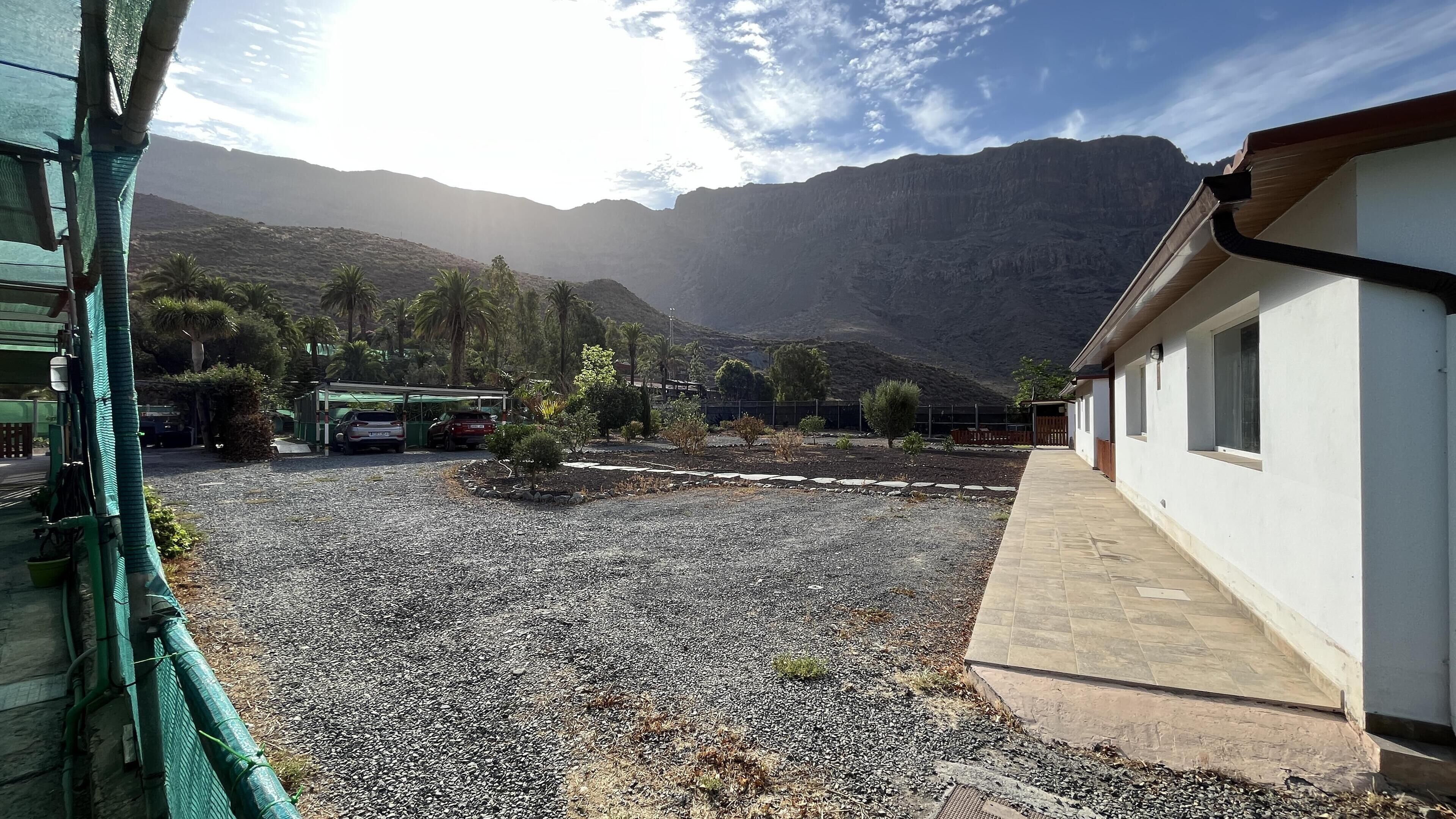 A gravel courtyard with parked cars, a white building, and a mountain backdrop.