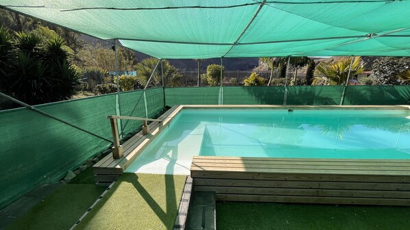 Ein rechteckiger Swimmingpool mit Holzterrasse und einem grünen Netz umzäunt.