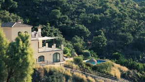 Une villa avec piscine, entourée d’une végétation luxuriante et de collines.