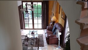 Un salon avec un canapé en cuir marron, une table à manger avec des chaises et un escalier menant à l’étage supérieur.