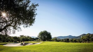 A golf course with a clear sky, a large tree, and distant mountains. - Casa Buganvilla 11 at Lauro Golf (Alhaurin de la Torre)