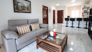 A living room with a grey sofa, a glass coffee table, and a painting on the wall. - Casa Buganvilla 11 at Lauro Golf (Alhaurin de la Torre)