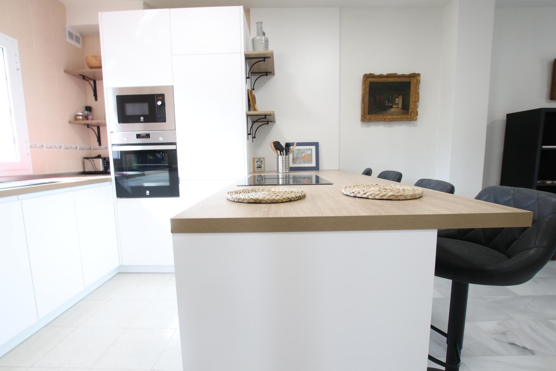 Une cuisine moderne avec des meubles blancs, un îlot central en bois et un coin repas avec des chaises.