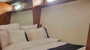 Een bed met wit beddengoed en een donkere deken, een houten hoofdbord en een klein lampje erboven.