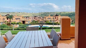 Une terrasse avec une table et des chaises, donnant sur une piscine et un quartier résidentiel avec des immeubles et des collines.