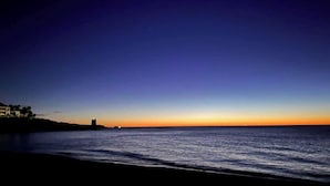 Un coucher de soleil sur la côte, avec une mer calme et une ligne de rivage lointaine.