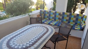 A balcony with a tiled table, a cushioned bench, and a view of greenery. - Apartmentsleeps4-pool-bbq-garden-ac (Manilva)