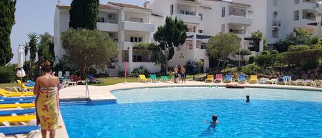 En swimmingpool med solstolar och en byggnad i bakgrunden.
