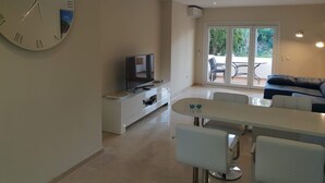 A modern living room with a large wall clock, a flat-screen TV, a dining table with chairs, and a sofa. - Apartmentsleeps4-pool-bbq-garden-ac (Manilva)