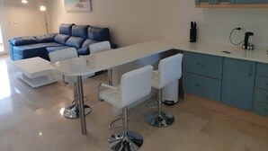 A modern living room with a sectional sofa, a dining table with bar stools, and a kitchen area with blue cabinets. - Apartmentsleeps4-pool-bbq-garden-ac (Manilva)
