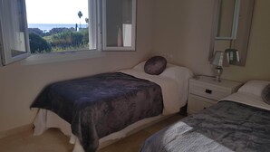 A bedroom with a bed, a bedside table with a lamp, a window with a view of the sea, and a mirror on the wall. - Apartmentsleeps4-pool-bbq-garden-ac (Manilva)
