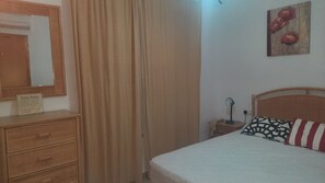 Et soveværelse med seng, natbord, lampe, spejl, kommode og et skilt med regler for toilettet.
