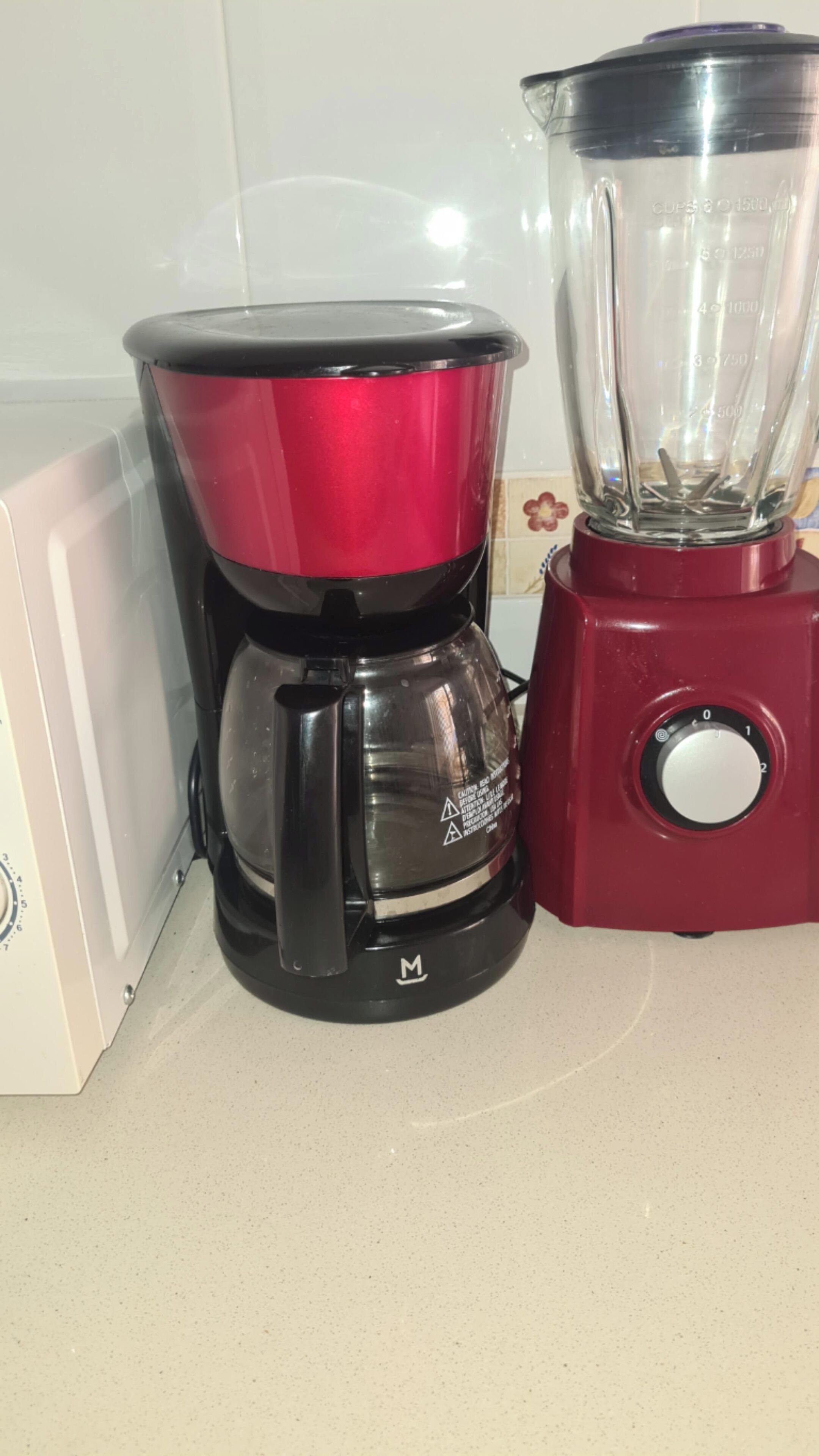A red coffee maker and a blender on a kitchen counter.