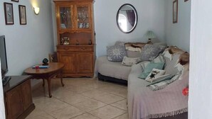 Ein Wohnzimmer mit einem Holzkasten, einem runden Spiegel, einer Couch mit Kissen und einem kleinen Tisch.