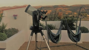 Ein Teleskop auf einem Stativ auf einem Dach mit Blick auf eine gebirgige Landschaft.