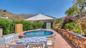 A pool area with a table and chairs, surrounded by stone walls and greenery. - Casa Redonda a Tranquil Spacious Apartment (Còmpeta)