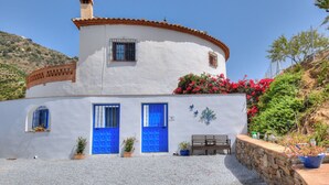 A white building with blue doors and windows, a stone bench, and potted plants. - Casa Redonda a Tranquil Spacious Apartment (Còmpeta)