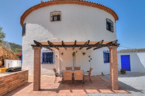 A white building with a blue door and windows, a covered patio with a table and chairs, and a brick column. - Casa Redonda a Tranquil Spacious Apartment (Còmpeta)