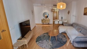 A modern living room with a grey sofa, a round coffee table, and a TV. There's a dining area with a table and chairs in the background. - Malaga Cityheart Stay Bright Modern City (Málaga)