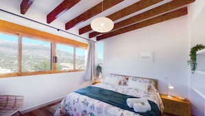 A bedroom with a bed, a nightstand, a lamp, a window with a view, and a hanging plant. - Sea View-2 Bed-sleeps 5-balcony-private Parking (Altea)