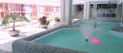 Une piscine avec une fontaine, entourée de murs recouverts de carreaux et de plantes en pot.