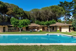 Ein Pool mit gefliestem Deck, ein überdachter Sitzbereich im Freien und ein Gebäude mit einem Ziegeldach.