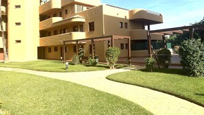A multi-story building with a curved facade, a covered outdoor area with seating, and a well-maintained lawn. - La Cala 2 Bedroom Apt With Sea View and Pool View (Mijas)