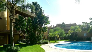 A pool area with a curved pathway, palm trees, and a building with balconies. - La Cala 2 Bedroom Apt With Sea View and Pool View (Mijas)