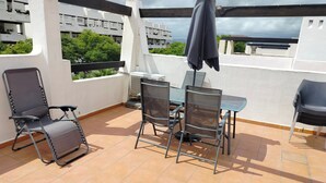 Une terrasse avec une table et des chaises, un appareil de climatisation et une vue sur les bâtiments et la verdure.