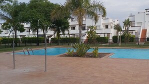 Une piscine avec une terrasse carrelée, entourée d’une clôture et bordée de palmiers.